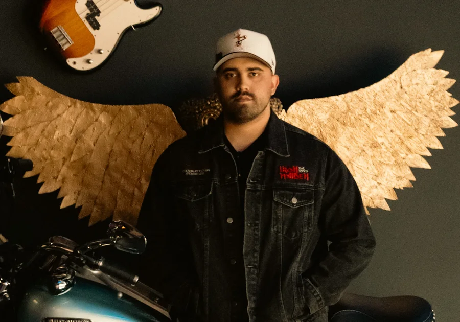André Martinho in front of golden wings, with a bass guitar and a Harley